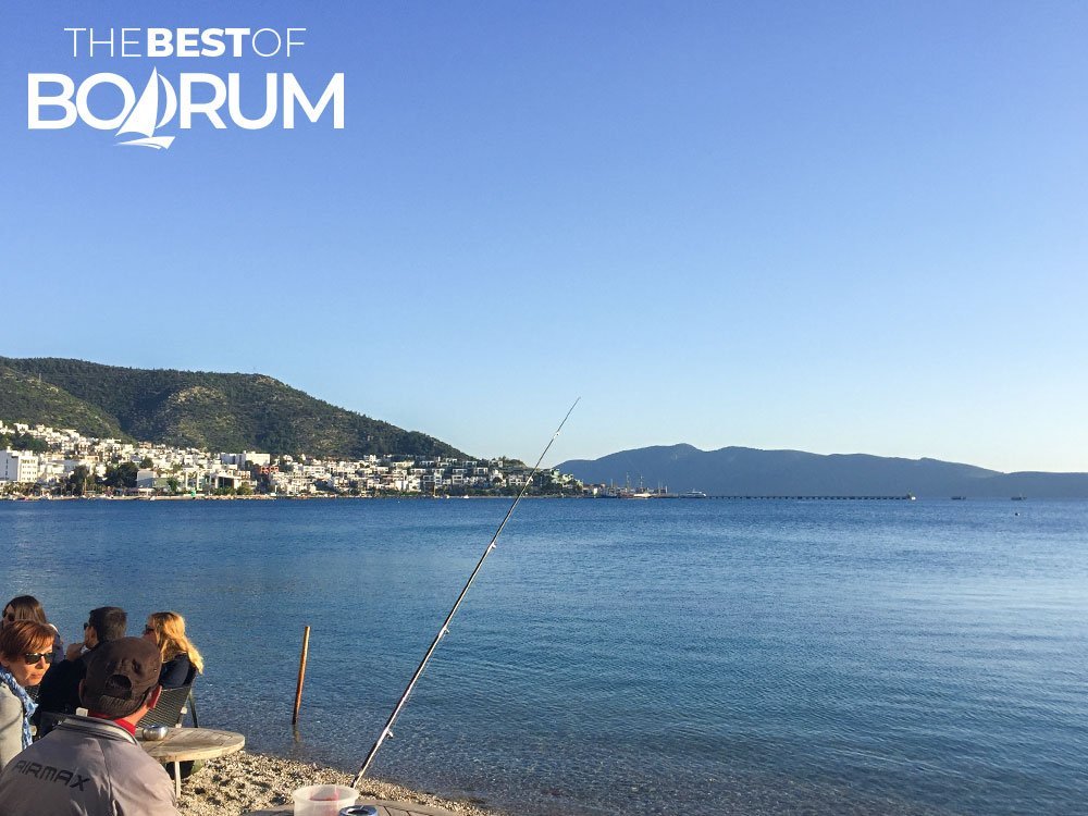 Bodrum coastline in January, people sitting at tables on the sandy beach.