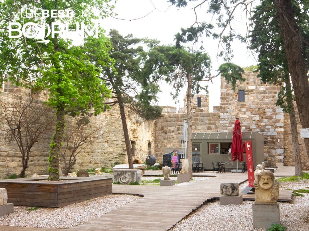 Bodrum Castle lower courtyard with trees, sculptures, and the Museum Café in the background.