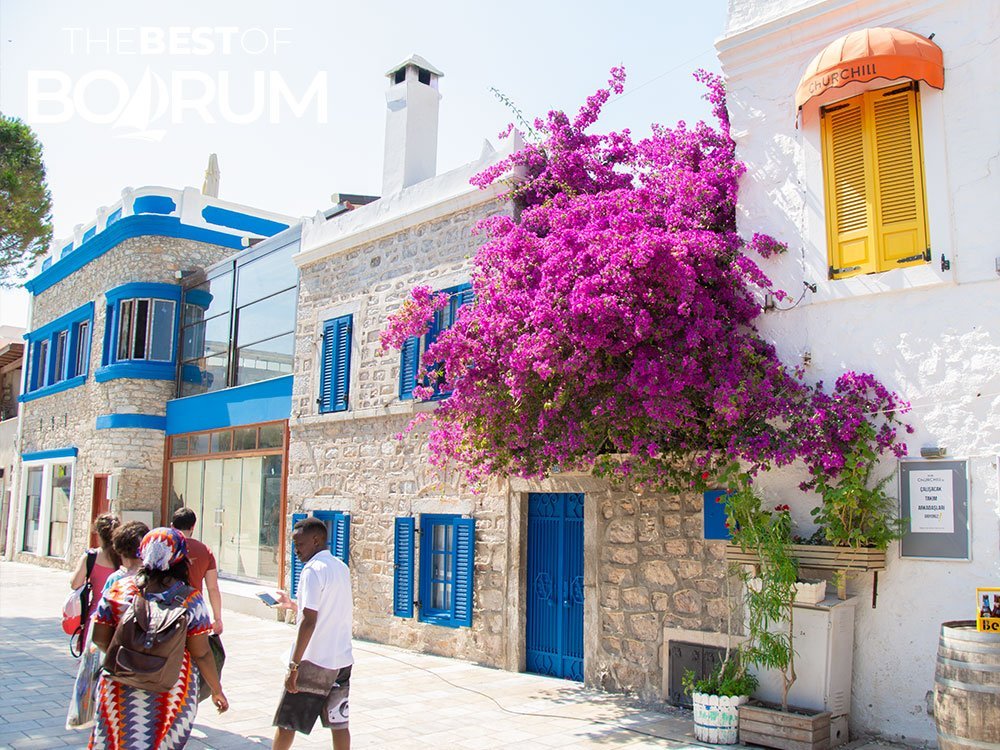 Visitors walking through Bodrum’s old town streets lined with stone houses and blooming bougainvillea.